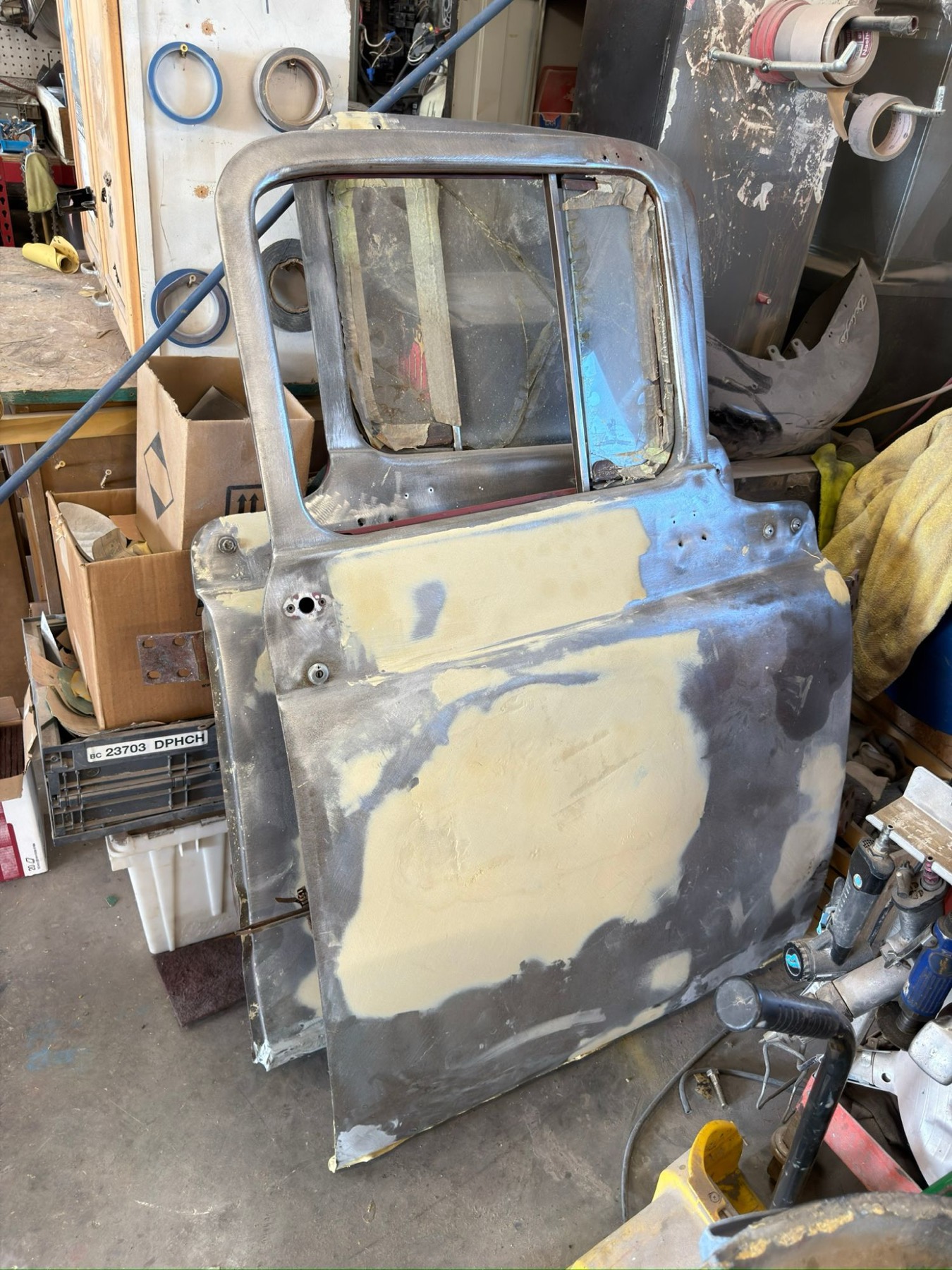 Truck door stripped to bare metal with body filler being shaped